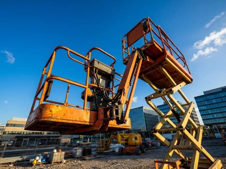 Oranje en gele hoogwerker met uitgeschoven platform tegen blauwe hemel op professionele bouwplaats