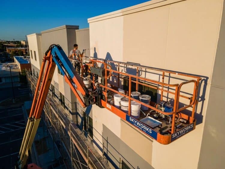 Oranje en blauwe hoogwerker met professionele schilderapparatuur bij gebouw tegen heldere hemel