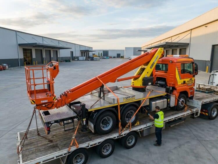 Hoogwerker met uitschuifbare giek op dieplader met spanriemen en veiligheidskettingen voor professioneel transport