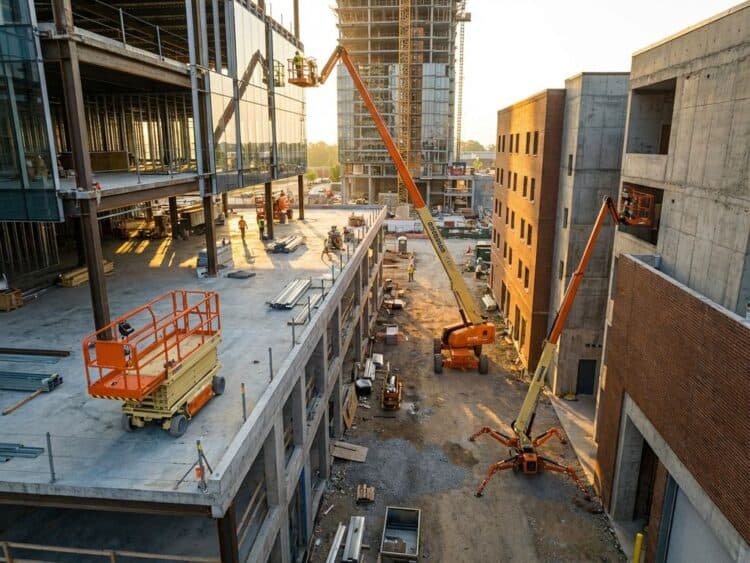 Luchtfoto van drie verschillende hoogwerkers op bouwplaats: oranje schaarlift, gele hoogwerker en spinhoogwerker
