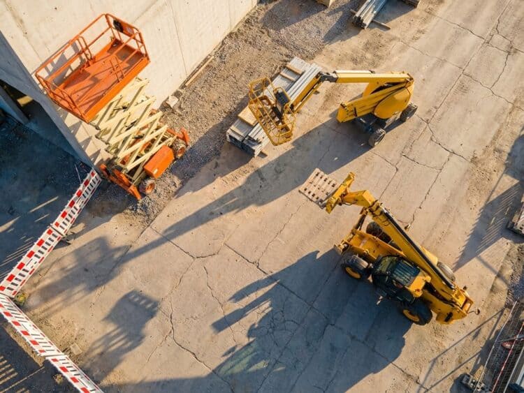Drie oranje en gele hoogwerkers op bouwplaats: schaarliften, telescoopkraan en giekliften in driehoeksformatie
