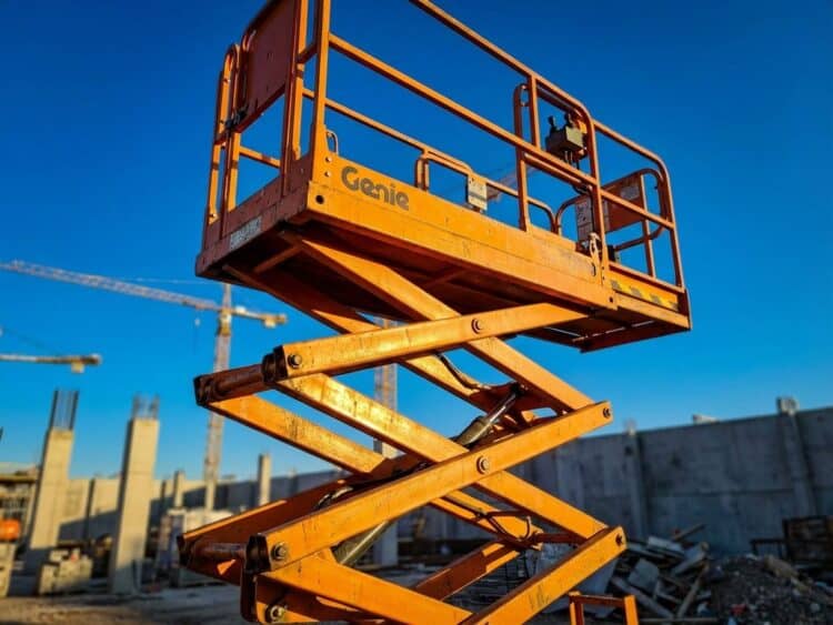 Oranje schaarlift platform verhoogd tegen blauwe hemel, met kenmerkende schaar mechanisme en stalen constructie