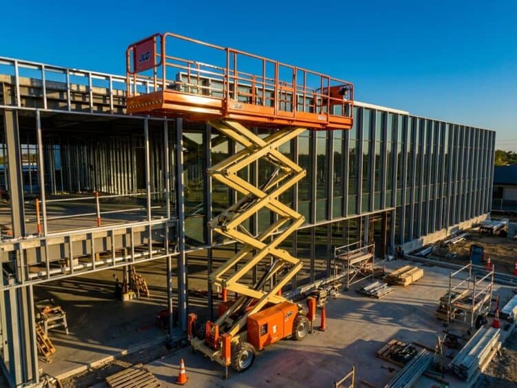Oranje schaarlift verhoogd naast modern gebouw in aanbouw met bouwmaterialen op betonnen ondergrond