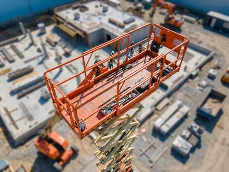 Oranje schaarlift werkplatform op hoogte met veiligheidsreling en ruime werkruimte op bouwplaats