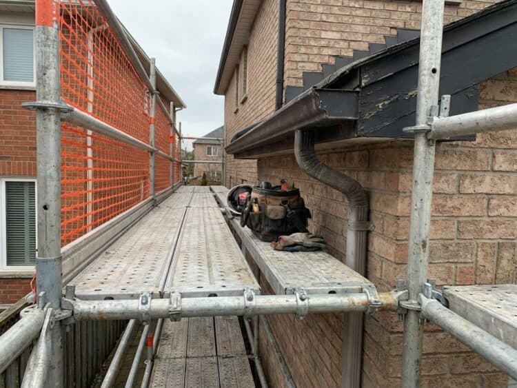 Industriële steiger tegen dakgoot met aluminium palen, veiligheidsrails en werkplatform voor onderhoud