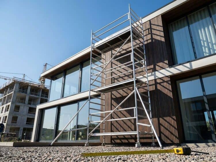 Aluminium steiger tegen modern huis, gefotografeerd vanuit lage hoek met meetlint op voorgrond voor hoogtebepaling