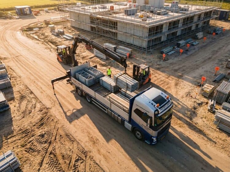 Professionele vrachtwagen levert modulaire stalen steigermaterialen op bouwplaats tijdens gouden uur