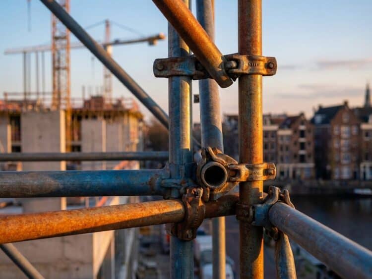 Industriële steigerbuizen en klemmen in geometrische patronen op bouwplaats tijdens gouden uur met dramatische schaduwen