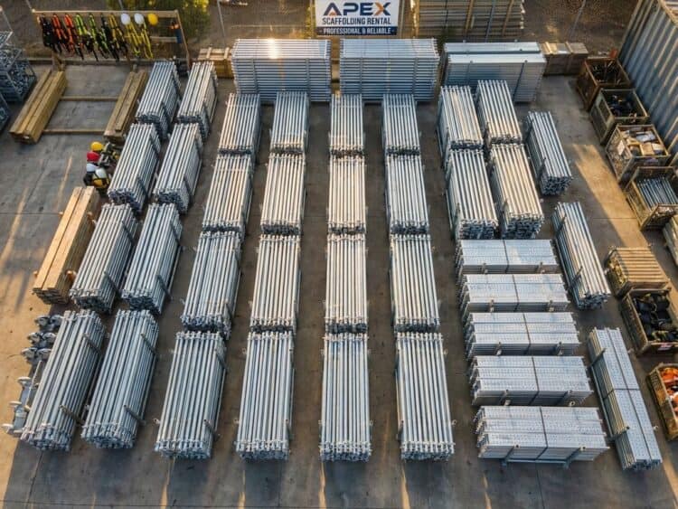 Industriële steigermateriaal georganiseerd op betonnen erf met aluminium buizen, verbindingen en platforms in zonlicht