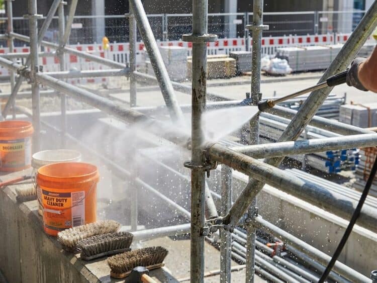 Metalen steigerbuizen worden schoongemaakt met hogedrukspuit, waterdruppels en reinigingsapparatuur zichtbaar op bouwplaats