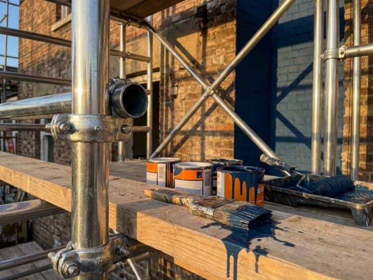 Professionele steigeruitrusting met verfkwasten en verfblikken op houten plank bij bouwproject