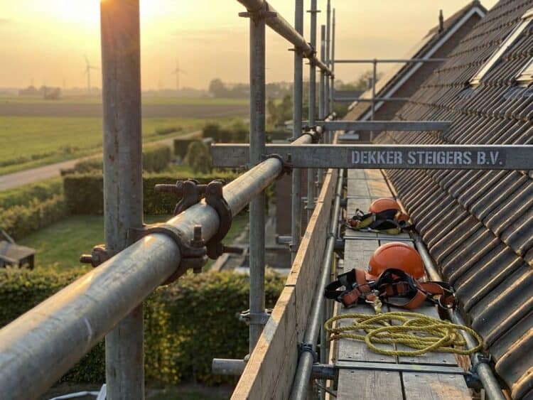 Professionele steigers tegen woonhuis dak met stalen buizen, veiligheidshekken en oranje bouwgereedschap