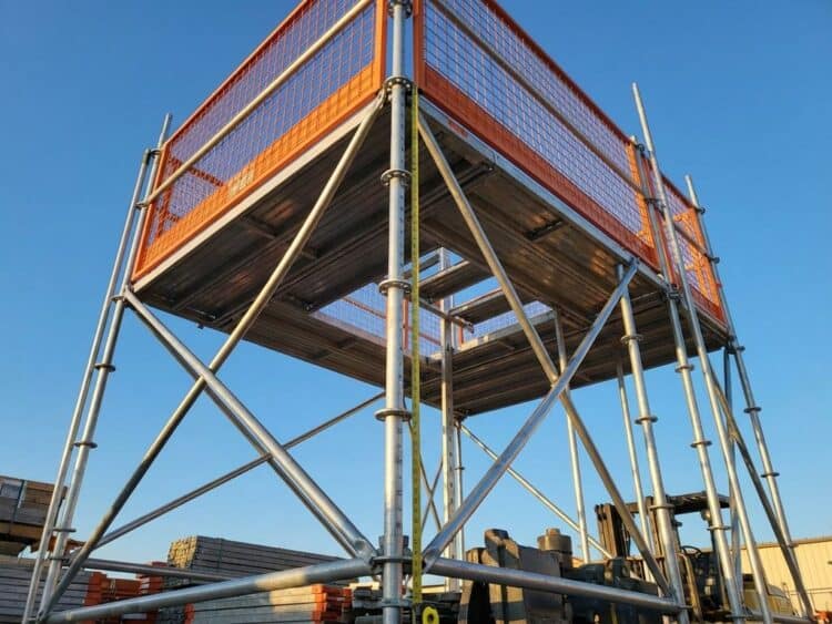 Hoge aluminium steiger met oranje veiligheidsbarrières tegen blauwe hemel, dramatische schaduwen benadrukken industriële schaal