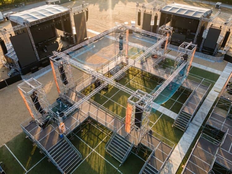 Professionele steigerstructuren rond evenementlocatie tijdens gouden uur, met podiumplatforms en geometrische patronen