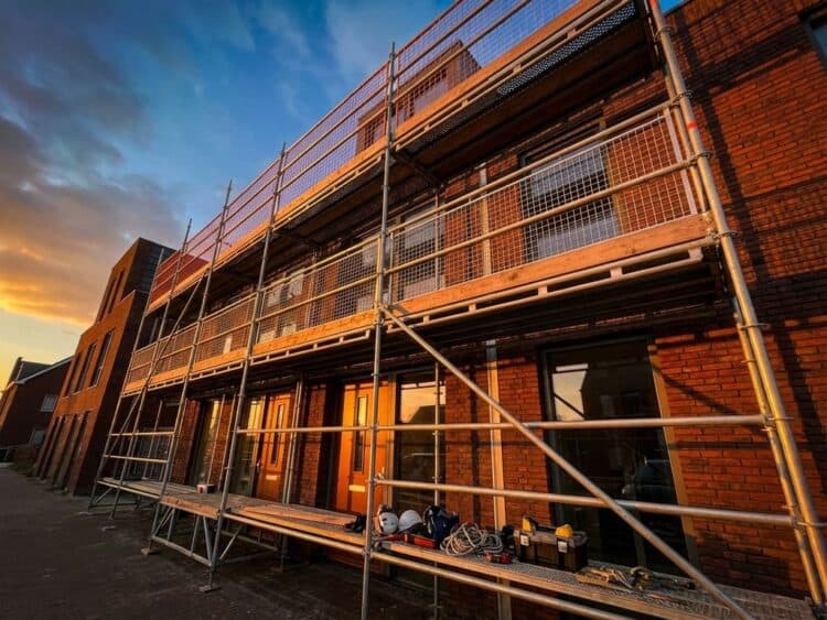 Professionele stalen steiger met veiligheidsrails tegen moderne Nederlandse woning tijdens gouden uur