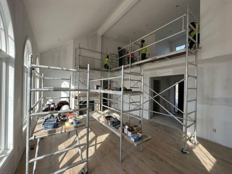 Professionele steiger in moderne woonkamer tijdens renovatie met gereedschap en natuurlijk licht door grote ramen