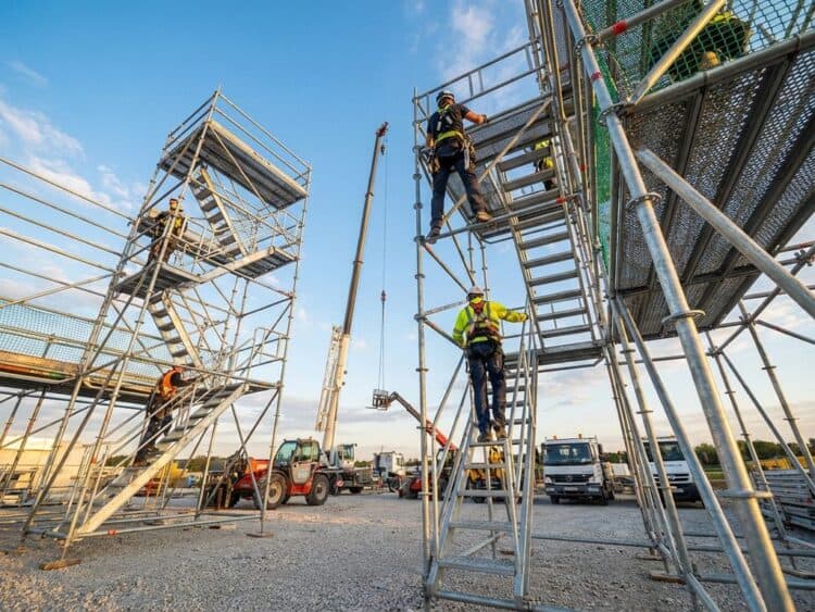 Professionele steigerwerkers assembleren metalen steiger tegen blauwe hemel, constructievoertuigen op werkterrein