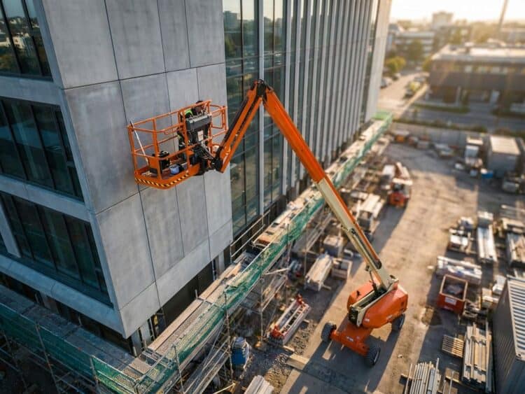 Oranje telescopische hoogwerker uitgeschoven tegen gebouwgevel in renovatie, met veiligheidsmaterialen op de grond