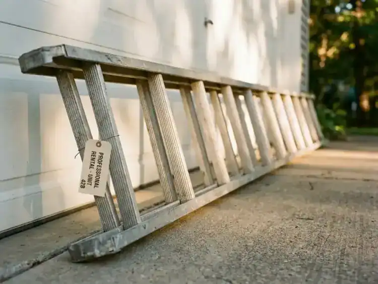 Aluminium uitschuifladder tegen witte garagemuur op betonnen oprit met zachte namiddagschaduwen