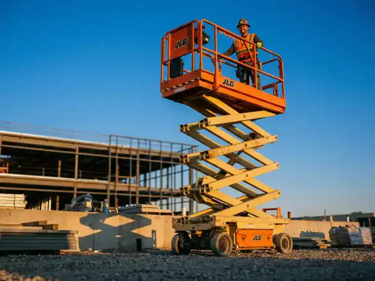 Oranje schaarlift volledig uitgeschoven tegen heldere blauwe hemel, bouwvakker in veiligheidsvest bedient platform