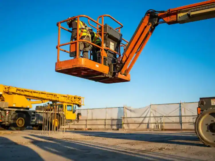 Oranje schaarlift met operator in veiligheidsuitrusting op bouwplaats, gele kraan en witte steiger op achtergrond